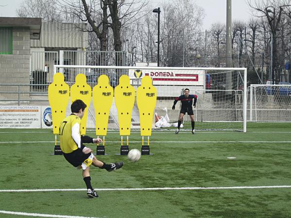 Fußballspieler schießt Freistoß auf Torwart hinter gelben Trainingspuppen auf Fußballfeld.