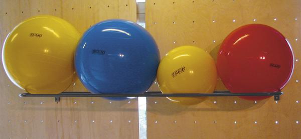 Verschiedene bunte Gymnastikbälle in Gelb, Blau und Rot auf einem Regal vor Holzwand.