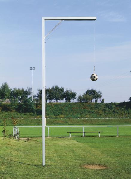 Trainingsgerät mit hängendem Fußball auf grünem Fußballfeld bei klarem Himmel.