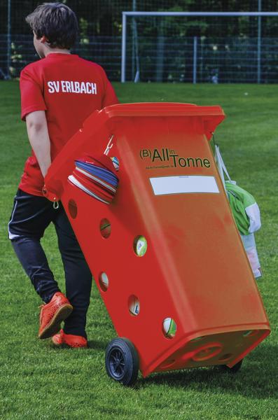 Junge in rotem SV Erlbach Shirt zieht eine orange Balltonne auf dem Fußballfeld.