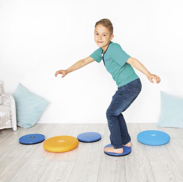 Junge balanciert auf bunten Balance-Discs im Wohnzimmer, spielerisch Koordination trainierend.