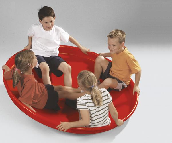 Vier Kinder sitzen lachend auf einem roten Spielgerät und drehen sich gemeinsam.