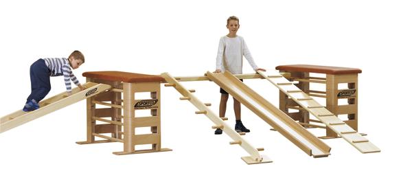 Kinder spielen auf einem Holz-Klettergerüst mit Rampen und Sprossenleitern in der Turnhalle.
