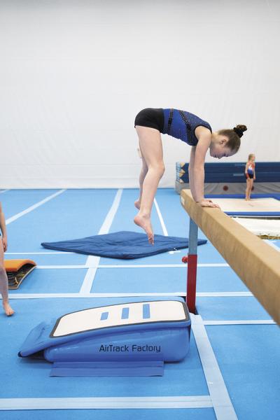Mädchen trainiert Handstand am Schwebebalken in Turnhalle mit blauen Matten.