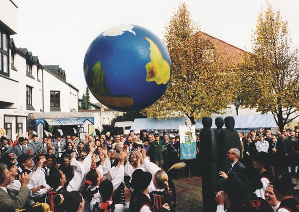 Menschen spielen mit großer Weltkugel bei traditionellem Fest im Dorf.