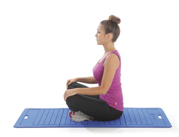 Frau in Sportkleidung sitzt im Schneidersitz auf blauer Yogamatte, meditiert entspannt.