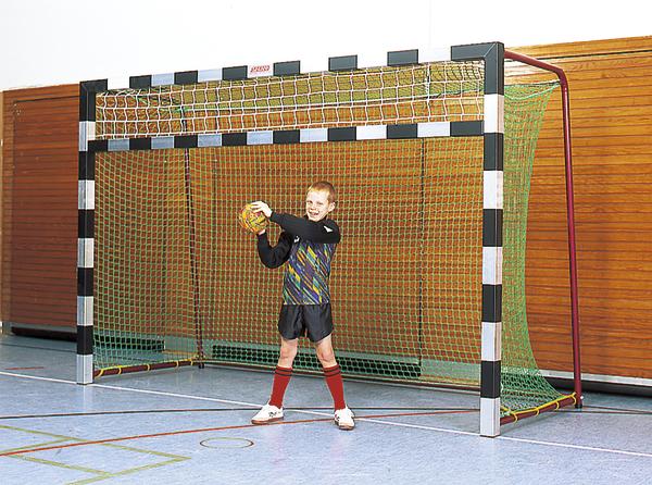 Junge als Handballtorwart hält Ball vor Handballtor in Sporthalle.