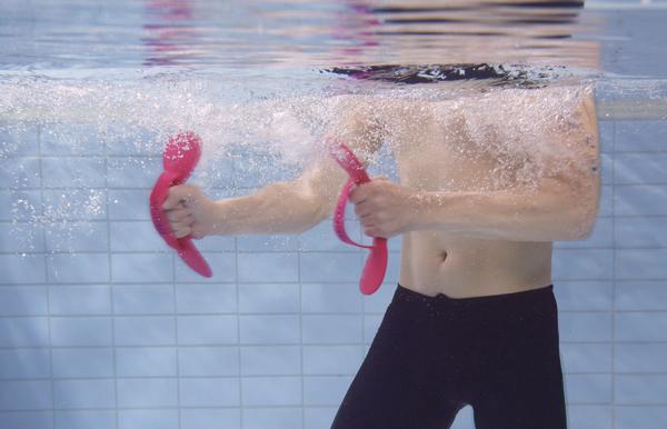 Mann trainiert Unterwasser mit roten Fitnessgriffen im Schwimmbecken.