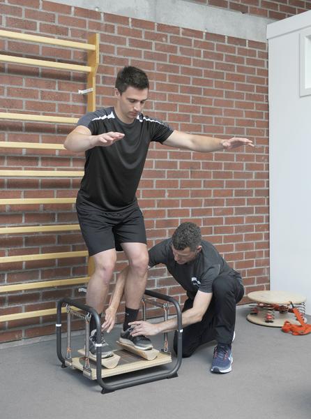 Mann trainiert Gleichgewicht auf Wackelbrett, Trainer unterstützt in Fitnessstudio mit Kletterwand.