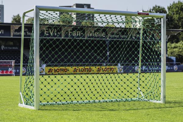 Fußballtor mit grünem Netz auf gepflegtem Rasen in einem Stadion bei Tageslicht.