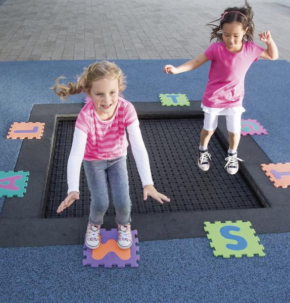 Zwei Mädchen springen fröhlich auf einem Trampolin im Außenbereich mit bunten Buchstabenmatten.