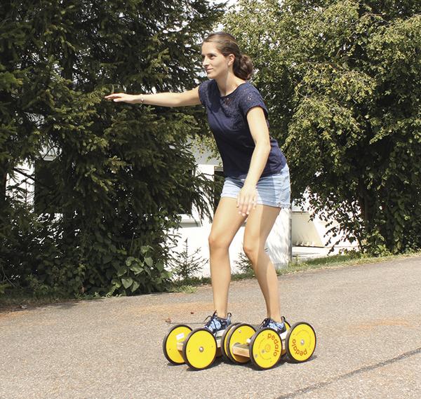 Frau fährt auf gelbem Rollbrett mit vier Rädern auf Asphaltweg im Freien.