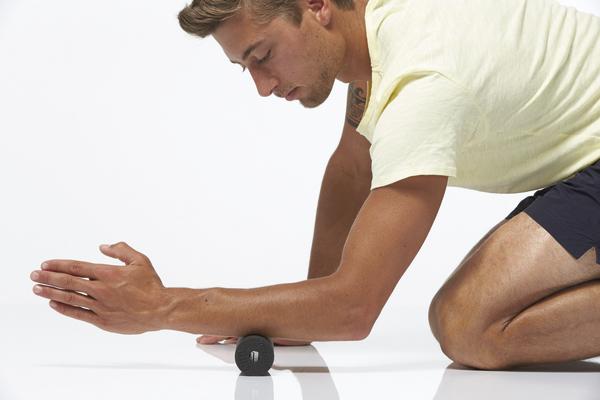 Mann führt eine Massageübung mit einer kleinen Faszienrolle am Unterarm durch.