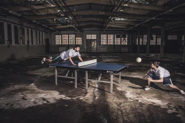 Zwei Männer spielen Tischtennis in einer verlassenen, großen Industriehalle.