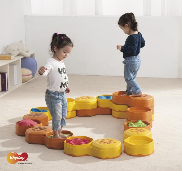 Zwei Kinder balancieren auf bunten, modularen Spielbausteinen in einem hellen Raum.
