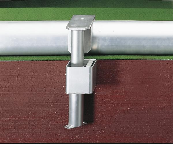 Metallhalterung zur Befestigung eines weißen Rohres an einer roten Wand mit grünem Hintergrund.