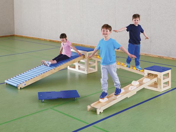 Kinder spielen auf einem Indoor-Kletterparcours mit Balancier- und Rutschgeräten in der Turnhalle.