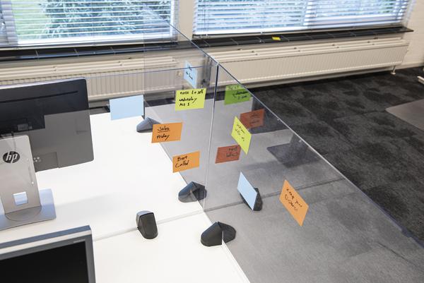 Büroarbeitsplatz mit Computer und bunten Haftnotizen an einer Glaswand als Organisationshilfe.