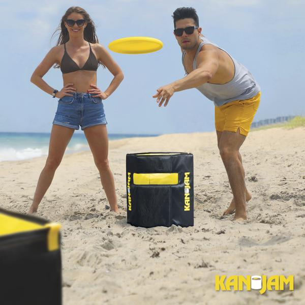 Mann und Frau spielen mit einer gelben Wurfscheibe am Strand, zwischen ihnen steht ein schwarz-gelber KanJam-Behälter.