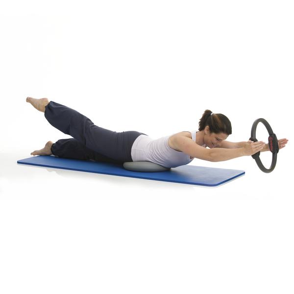 Frau macht Pilates-Übung mit Pilates-Ring auf blauer Matte zur Kräftigung der Rückenmuskulatur.
