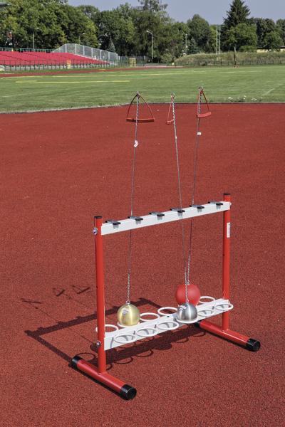 Sportgerät für Hammerwurf-Training auf roter Laufbahn im Freien mit grüner Wiese im Hintergrund.