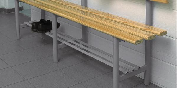 Sitzbank mit Holzlatten und Schuhablage aus Metall auf grauem Fliesenboden vor weißer Wand.