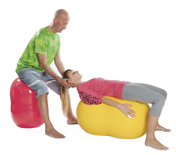 Mann unterstützt Frau bei Nackenentspannung auf Gymnastikbällen in Physiotherapie.