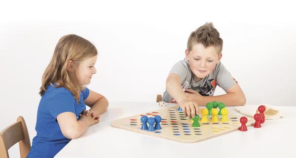 Zwei Kinder spielen Brettspiel mit bunten Spielfiguren an weißem Tisch.