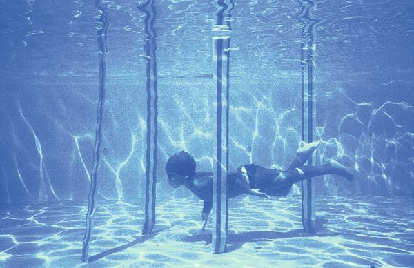 Kind taucht unter Wasser in einem Schwimmbecken mit Metallstangen und klarem Wasser.