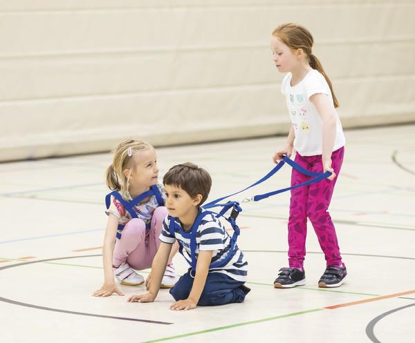 Drei Kinder spielen mit Zuggeschirr in der Turnhalle, zwei sitzen, eines zieht.