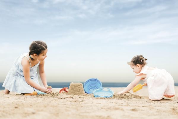 Kinder bauen Sandburg am Strand mit Spielzeug unter blauem Himmel.