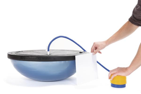 Person pumpt Balance-Trainingsgerät mit gelber Fußpumpe auf weißem Hintergrund.