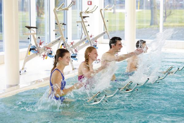 Vier Personen beim Aquafitness-Training im Hallenbad mit Wasserspritzern.