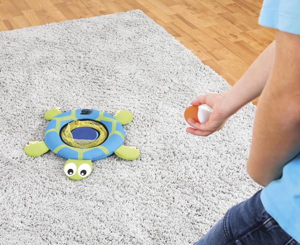 Kind spielt mit Wurfspielzeug in Schildkrötenform auf grauem Teppichboden.