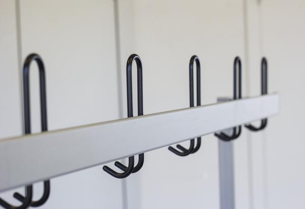 Moderner weißer Garderobenständer mit schwarzen Haken vor weißer Wand.