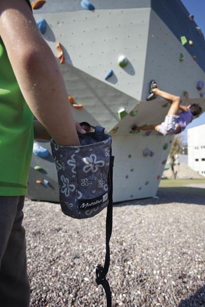 Kletterer mit Chalkbag im Vordergrund, Kind klettert an Outdoor-Kletterwand bei Sonnenschein.