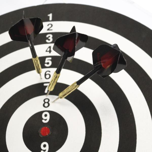Drei Karella Steeldarts mit goldfarbenen Barrels und schwarzen Flights stecken in einer schwarz-weißen Trainings-Zielscheibe mit nummerierten Ringen.