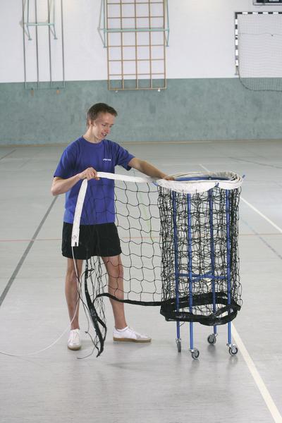 Junger Mann montiert ein Sportnetz an einem mobilen Ballwagen in der Turnhalle.