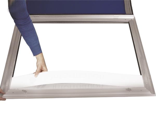 Person legt ein weißes Blatt in einen Schaukasten ein.