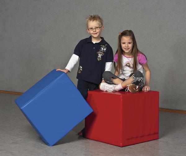 Zwei Kinder mit Spielwürfeln, Junge steht mit blauem Würfel, Mädchen sitzt auf rotem Würfel.