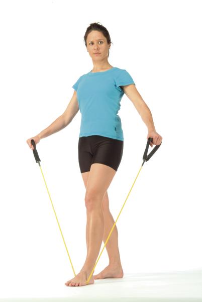 Frau trainiert mit Widerstandsband im Stehen, trägt blaues Shirt und schwarze Shorts.