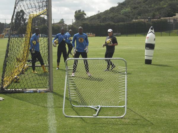 Torwarttraining auf Fußballfeld mit mehreren Spielern und Trainingsgerät im Vordergrund.