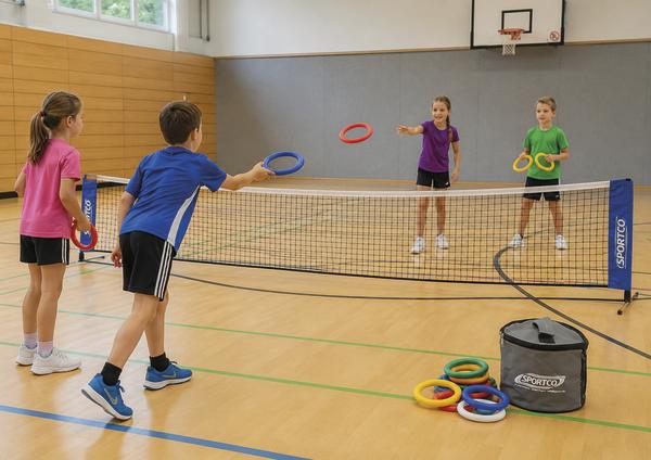 Vier Kinder beim gemeinsamen Wurfspiel mit bunten Ringen über ein Netz in einer Sporthalle.