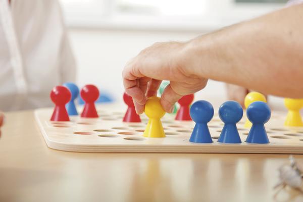 Hand bewegt gelbe Spielfigur auf Holzspielbrett mit bunten Figuren beim Brettspiel.