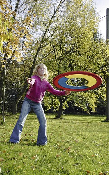 Kind wirft bunten Frisbee im sonnigen Park mit grünen Bäumen im Herbst.