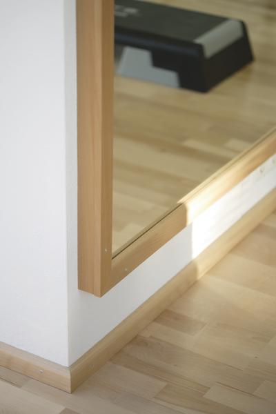 Eckspiegel mit Holzrahmen und Parkettboden in hellem Raum.