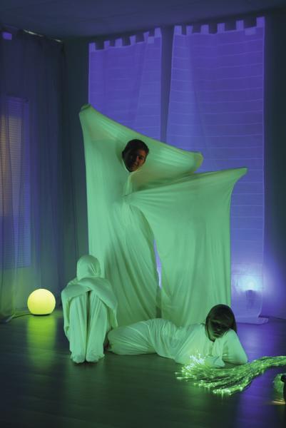 Drei Personen in leuchtenden grünen Tanzsäcken in einem dunklen Raum mit blauem Licht.