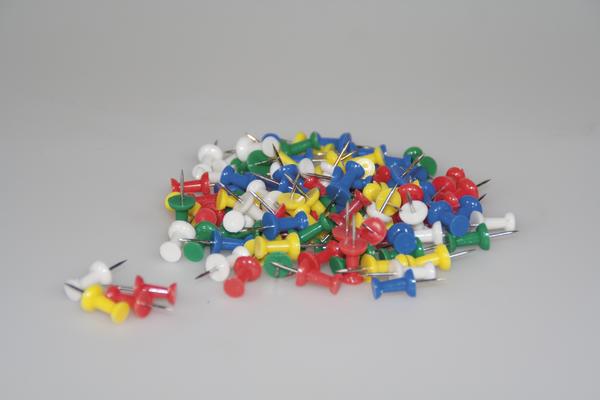 Bunte Reißzwecken in verschiedenen Farben auf grauem Hintergrund, Bürobedarf.