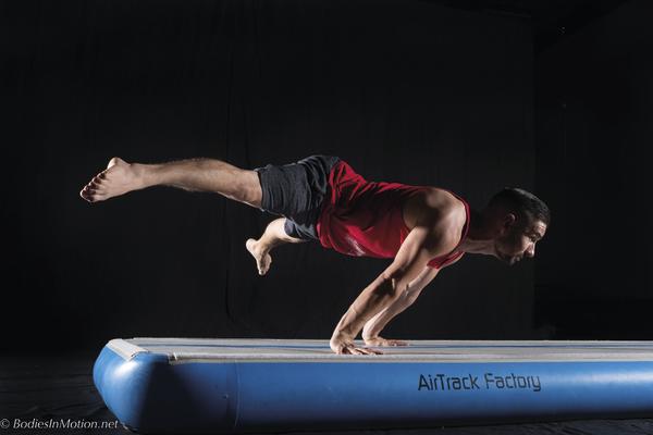 Mann führt fortgeschrittene Gymnastikübung auf AirTrack Matte in Sportstudio aus.