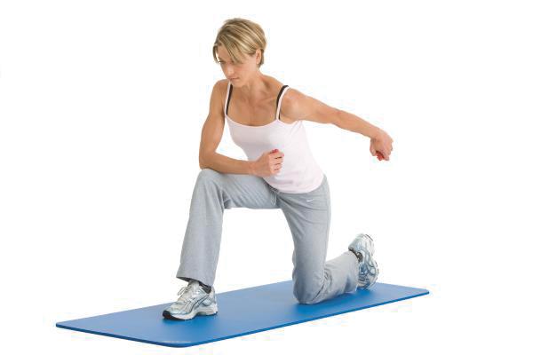 Frau macht Dehnübung auf blauer Fitnessmatte, trägt Sportkleidung und Sportschuhe.